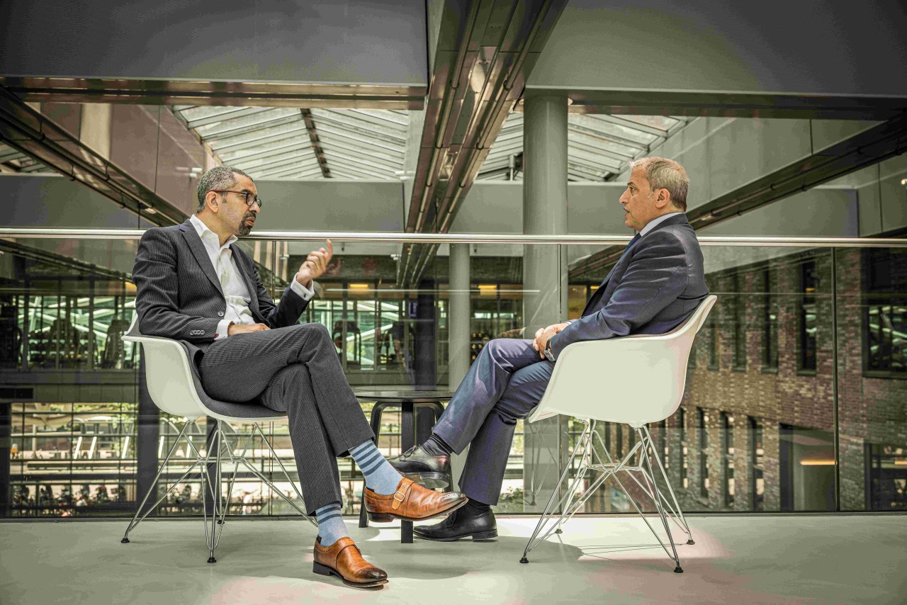 2 smart men conversing while sitting on 2 white chairs.