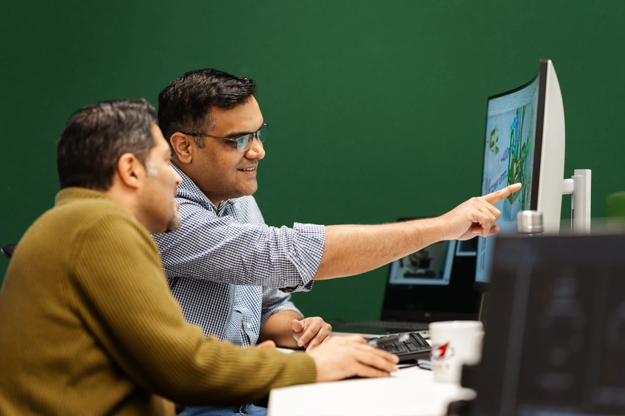 2 man checking a drawing on the computer with a green background wall.