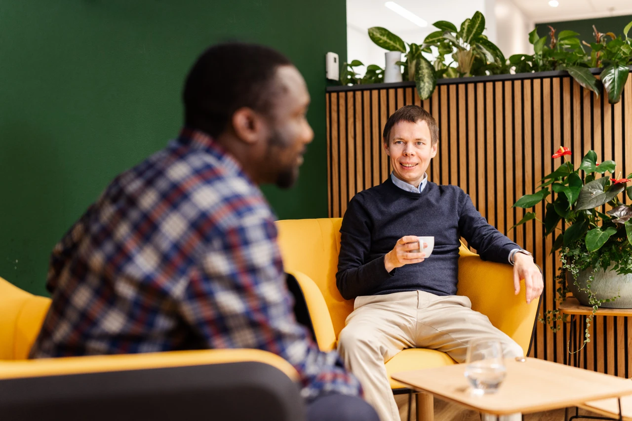 2 smiling sitting on 2 yellow armchairs with plants on the background.