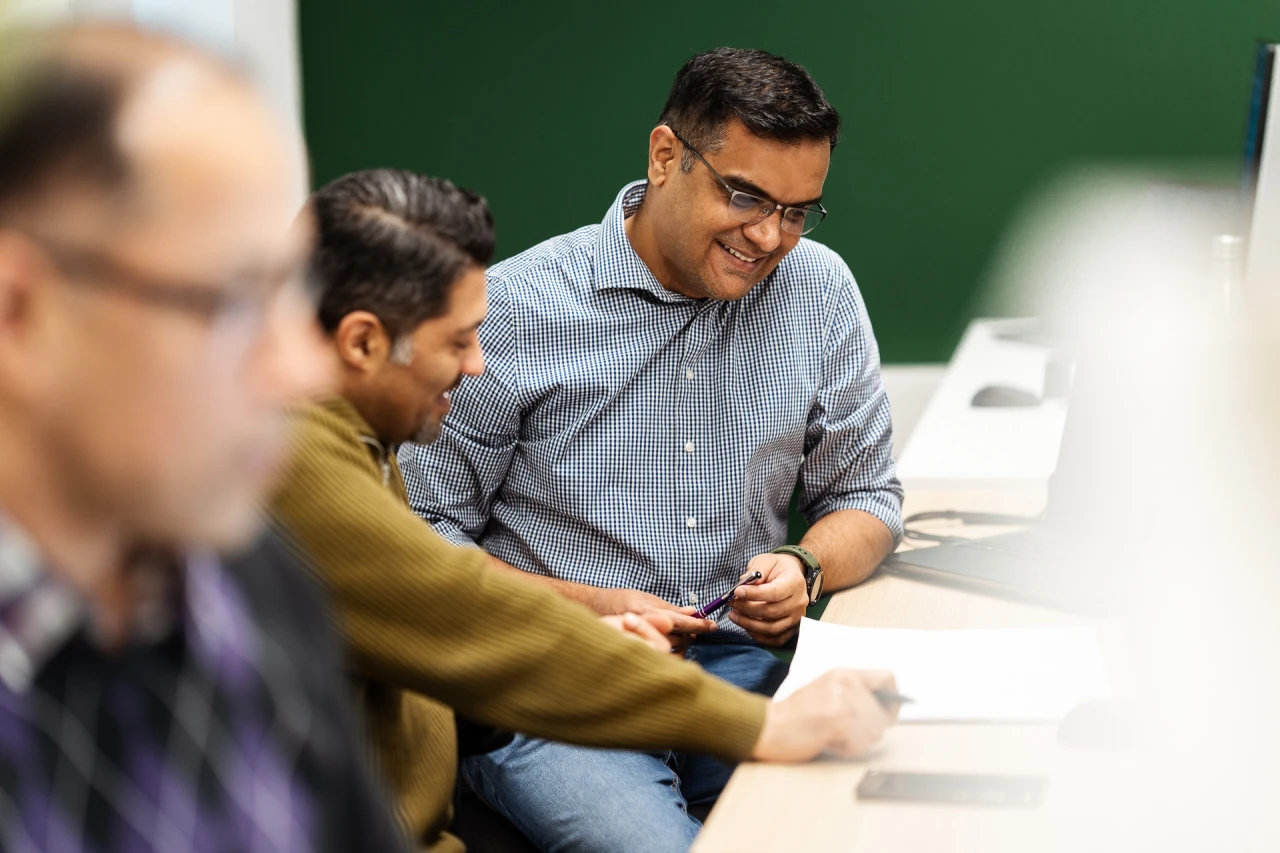 2 man smiling and holding 2 pens while checking a documents.