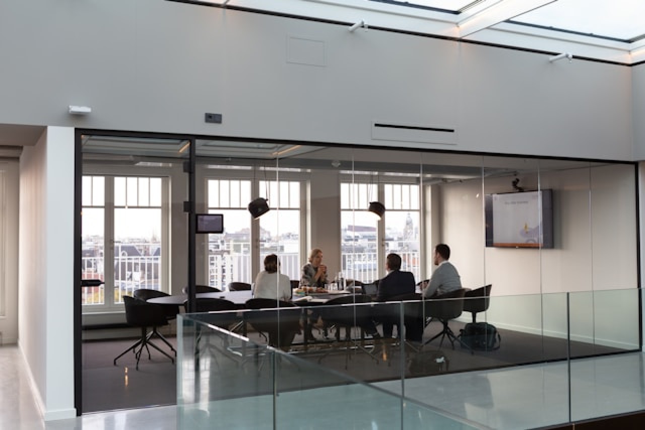 4 people sitting in a meeting room with a big screen on the wall conversing with each other.