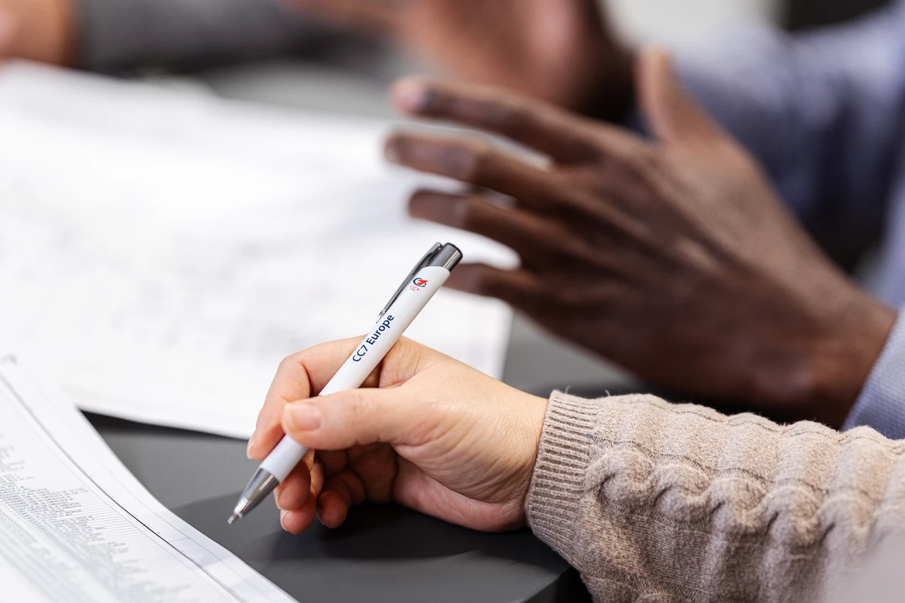 2 hands and 1 is holding a branded pen.